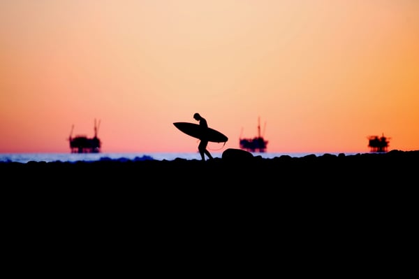 Surfer walking in front of refineries